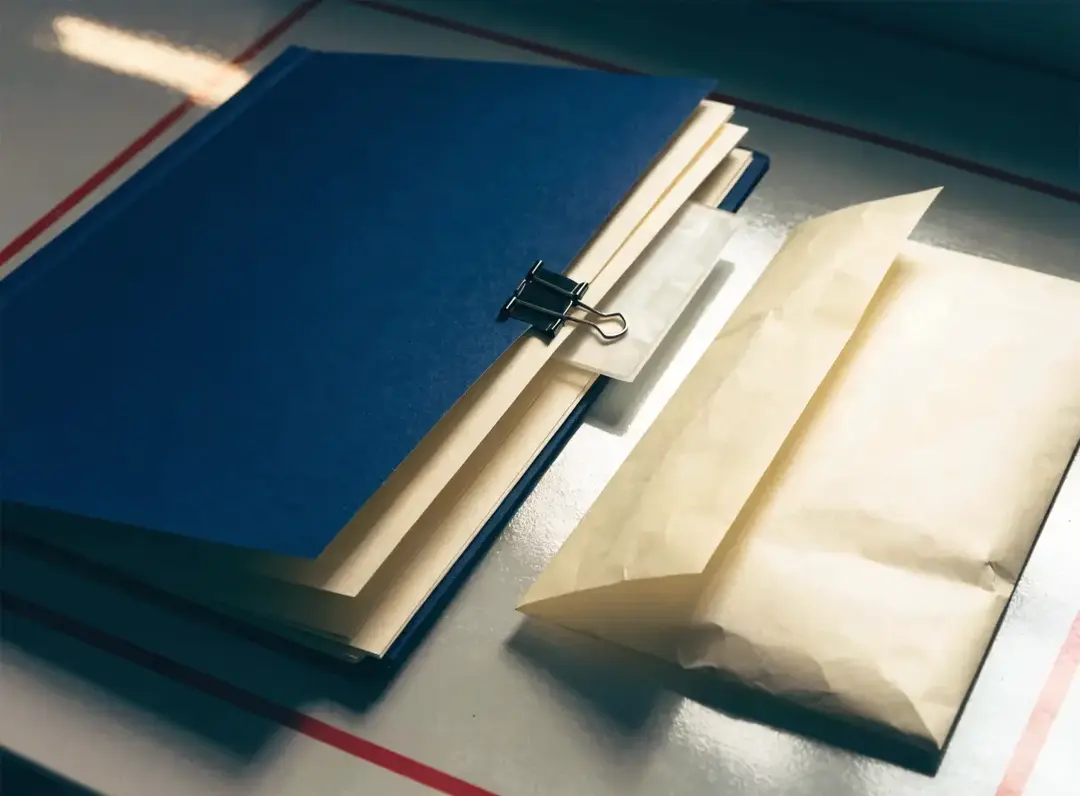 A compact blue handover folder, blank sheets, and an unmarked envelope inside a red boundary